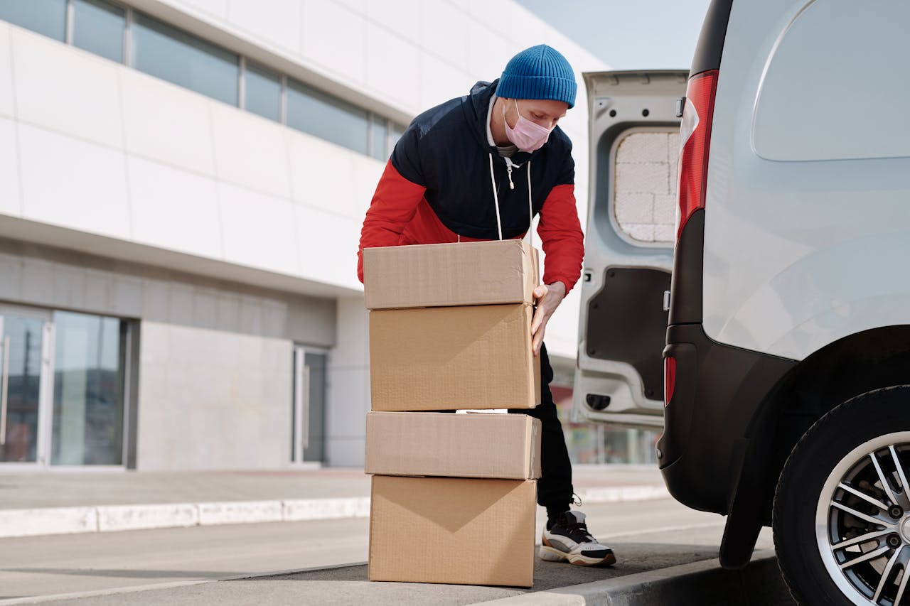 services-04 Delivery worker wearing a face mask loads boxes into a van, reflecting pandemic precautions.